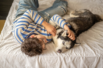 Teenager and husky lying together on same wide pillow, years of friendship turned into simple habit, image made for honest content marketing. Wide shot. Concept of friendship between teenager and dog © iwavephoto