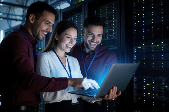 Group of professionals analyze data on laptop in modern server room. Diverse tech team works together on cloud infrastructure maintenance. Male engineer, female specialist monitor network system,