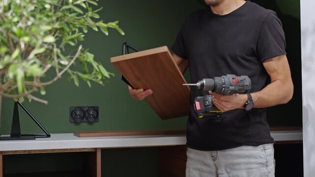 Man preparing a wooden shelf and cordless drill for mounting it on the wall