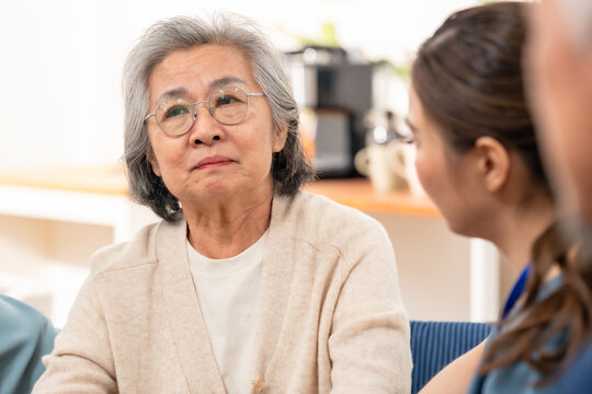 Senior Asian woman discusses health concerns with female nurse in assisted living center, receiving compassionate listening, emotional support, wellness guidance and reassuring nursing care.