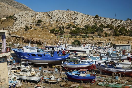 Many boats are moored in a shipyard in front of a mountainous landscape, Pothia, main town, port, Kalymnos, Sponge Diving Island, Dodecanese, Greek Islands, Greece