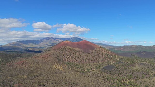 Aerial view of the volcanic Sunset Crater cinder cone surrounded by pine forests and rugged landscape in Coconino County, Arizona, United States.