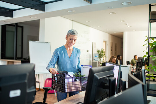 Smiling woman carrying box of belongings in office
