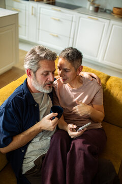 Middle-aged couple relaxing with smartphone and coffee at home