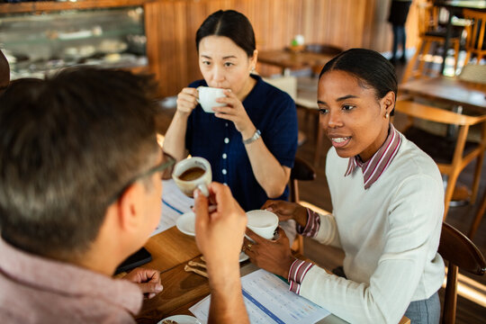Three colleagues discussing reports over coffee in a cafe