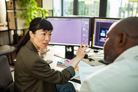 Designer explaining project to colleague at computer