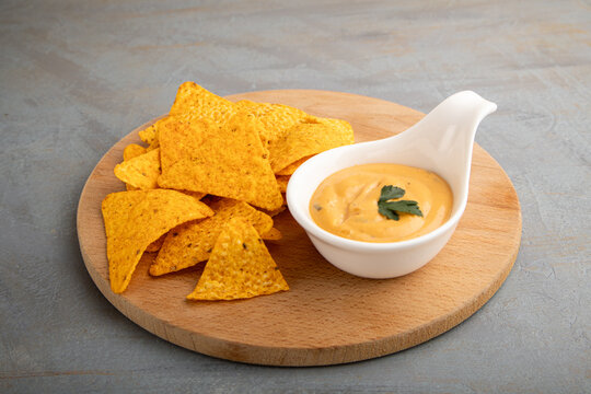 Tortilla chips and cheese dip on wooden board