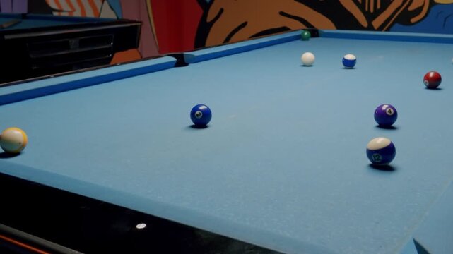 Focused player aiming and hitting the white cue ball with a pool stick on a blue felt table during a competitive match, showcasing precision, skill, and strategic gameplay in a sports bar