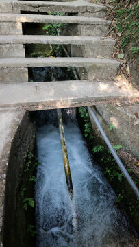 Fast flowing water stream flowing under concrete steps in rural area