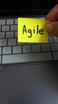 Hand holding agile sticky note over laptop keyboard