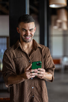 Happy male digital nomad checking smartphone while enjoying vacation at tropical resort