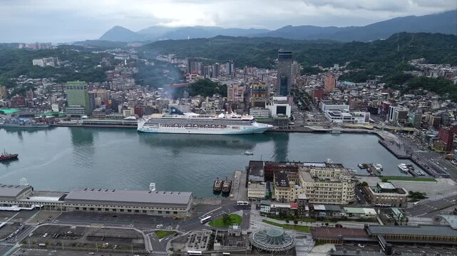 Aerial view above Keelung, which is a seaport city in northern Taiwan, with a cruise ship parking at the dock, vessels navigating in the harbor and off shore Keelung Islet standing on the horizon