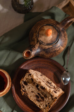 Piece of panettone bread on plate, teapot and cup on green linen tablecloth, sweet homemade bakery in rustic style, cottage core table setting