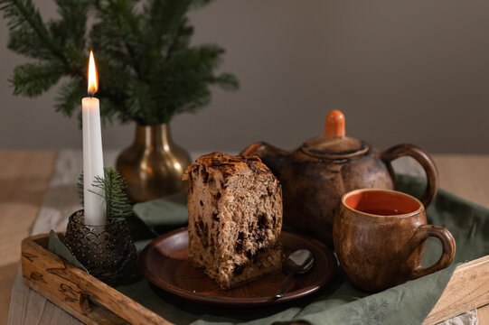 Panettone cake, teapot and cups, lighting candle and fir tree branches on wooden tray. Traditional Christmas bakery, table setting in cottage rustic style