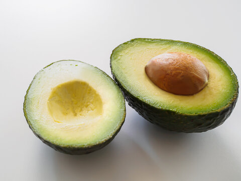Close-up of ripe avocado cut in half showing creamy flesh, green skin and brown pit on white background