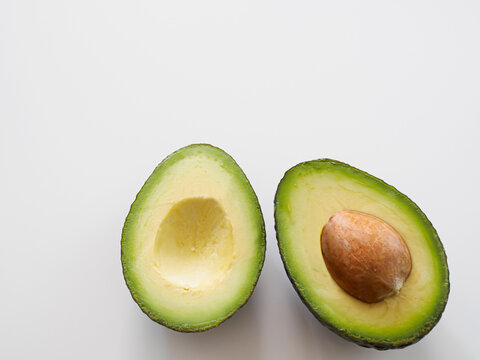 Avocado cut in half with pit on white background, fresh green fruit with copy space
