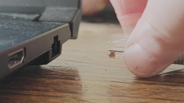 Close up view of a hand plugging and unplugging a gray ethernet lan cable into the port of a laptop for internet access