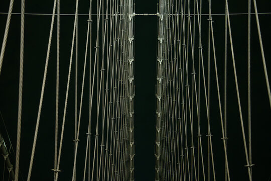Rows of suspension cables on the Brooklyn Bridge form a symmetrical pattern against the night sky in New York City. The illuminated structure highlights the engineering design of the historic landmark