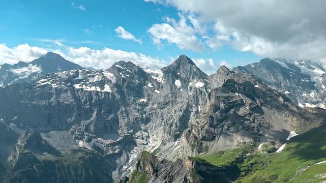 Jagged Swiss mountain range displays snowfields cliffs and green slopes, Clear summer panorama captures the rugged geology of the Bernese Alps