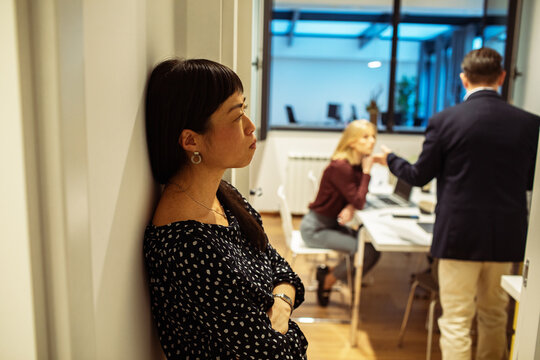 Woman leaning against wall during tense office meeting
