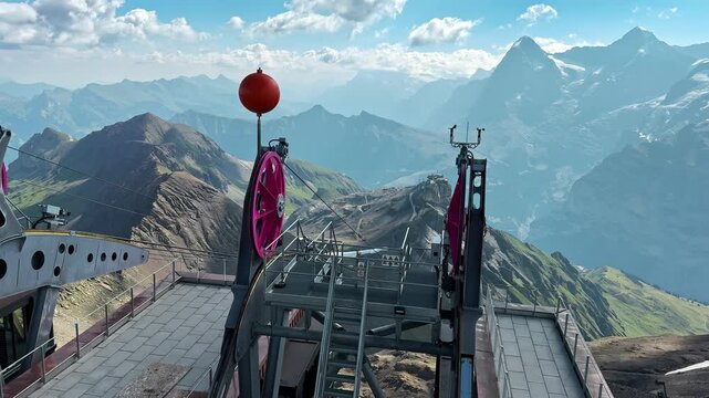 Mountain cable car station overlooks deep valleys in the Swiss Alps outdoors, High elevation infrastructure stands against distant snowy Alpine peaks