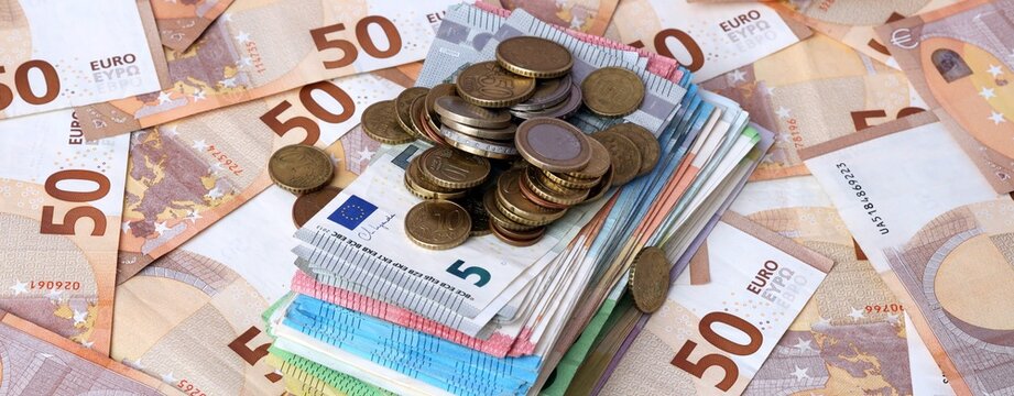 Pile of euro coins on stack of euro banknotes with fifty euro background