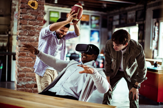 Men tease vr gamer with a football indoors