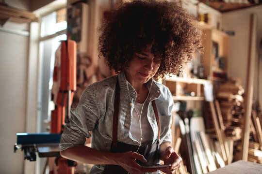 Female woodworker checking smartphone in workshop