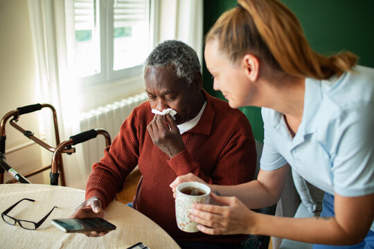 Caregiver offering tea to sick senior at home