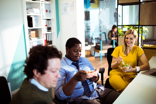 Coworkers eating lunch and chatting at office desk