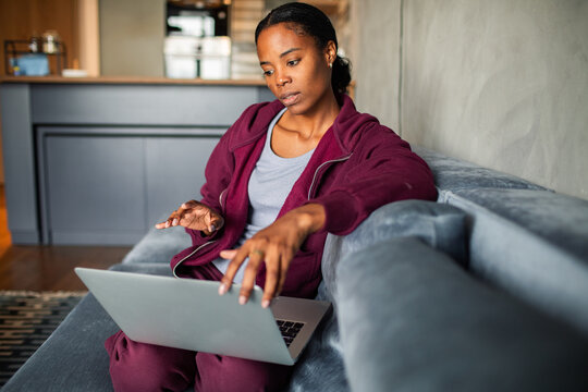 A pensive woman uses a laptop on the couch at home