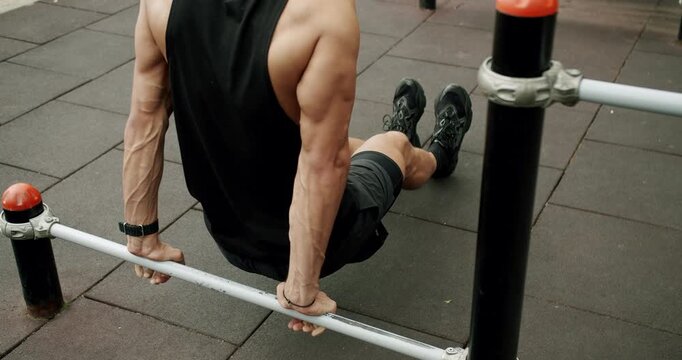 Sporty man has workout and doing reverse push up exercise on horizontal bar outdoors. Athlete male training arms muscles, biceps and triceps with gymnastic equipment at sport ground. Strength
