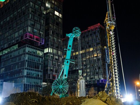 Construction processes at Piața Presei Libere metro station site in Bucharest featuring large drilling machinery and surrounding modern buildings at night