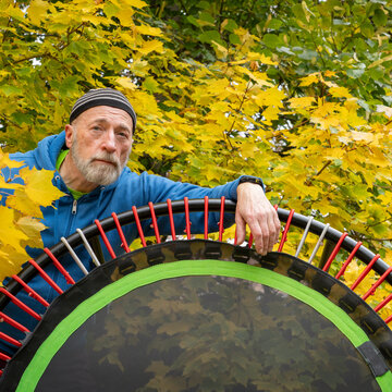 senior man with a mini trampoline for fitness exercising and rebounding, fall backyard  scenery