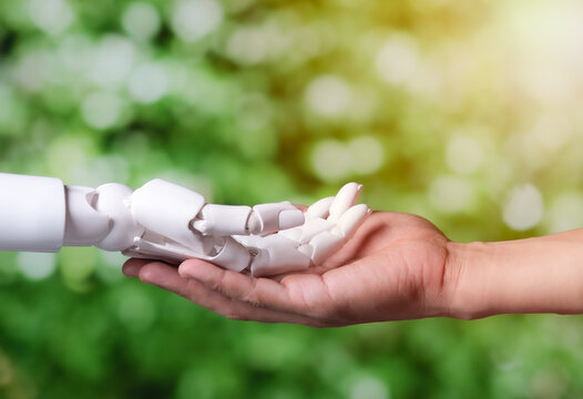 Human Hand Holding Robotic Hand on Green Nature Background for Eco AI Concept