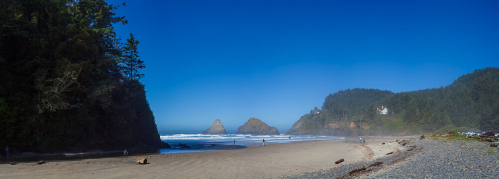 Beautiful wide panoramic view of a sandy ocean beach with green mountains, sea stacks and a historic house