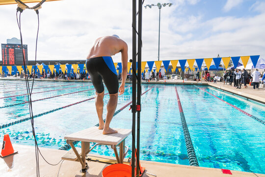 swimmer standing on diving block getting ready to race public pool