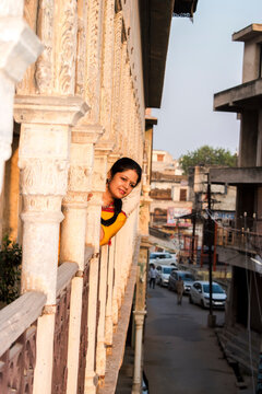 candid portrait of young woman in saree looking down toward the road as if waiting for someone, warm sunset light on her face