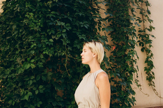 Woman Stands Beside Green Ivy Background in Sunny Location