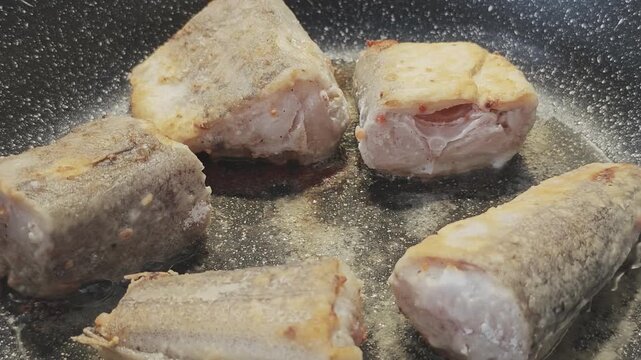 Delicious breaded fish pieces cooking in a dark pan. The hake is frying in hot, sizzling oil, creating a golden, crispy crust