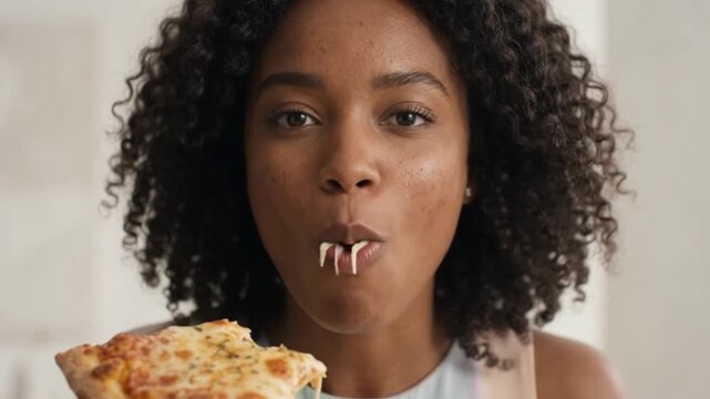 Young woman enjoys a cheesy slice of pizza, showing the delicious cheese pull and her happy expression