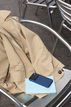 Smartphone and beige jacket placed on a metal chair outdoors