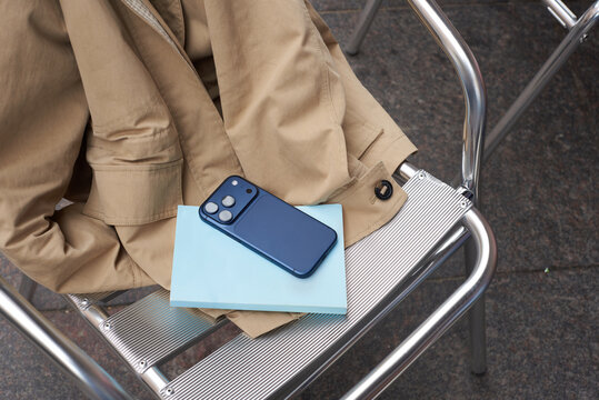 Smartphone, book and jacket lying on a metal chair.