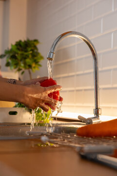 Hands washing  fresh red bell pepper under running tap water in modern kitchen sink. Close-up shot showing water splash, cleaning organic vegetables for healthy food cooking preparation Vertical