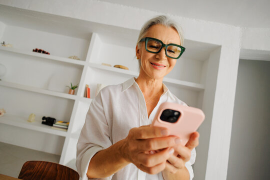 Senior woman smiling using smartphone at home