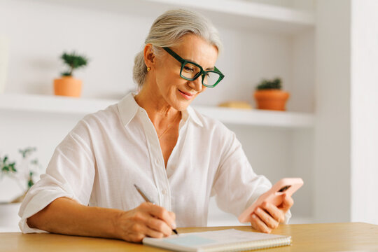 Senior woman planning schedule using smartphone and notebook