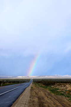 Rainbow stretching into the sky from the end of the highway vertical