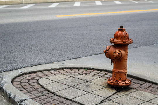 a weathered painted fire hydrant on a patterned stone sidewalk next to a paved street
