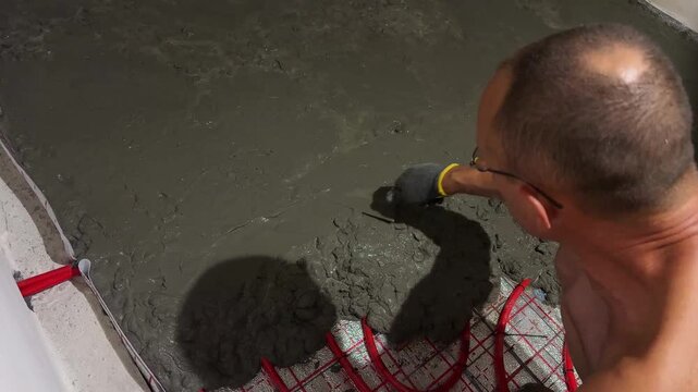 Worker leveling concrete screed over underfloor heating pipes, radiant floor installation