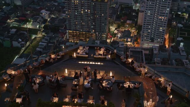 People enjoy rooftop party at a Bangkok sky bar with sprawling urban landscape at night and illuminated skyscrapers